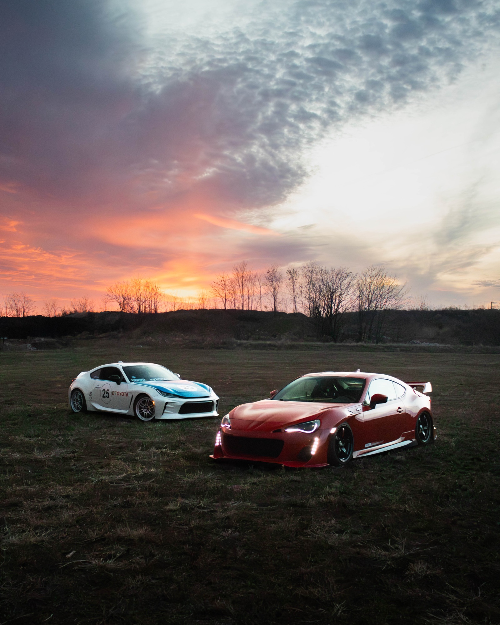 Two race-liveried coupes on a field at sunset